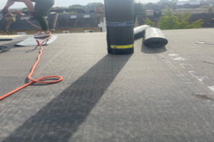 Worker installing a flat roof with a heat torch, with rolls of roofing material on the surface, done by ROU Roofing & Building Ltd.